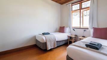 A bedroom with two beds, a window with curtains, and a wooden floor.