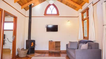 Ein gemütliches Wohnzimmer mit Kamin, Holzbalken, Fernseher und einer Couch.