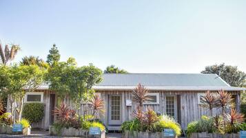 A building with a corrugated metal roof, wooden walls, and multiple entry points. There are signs indicating reserved parking for Garden Studios 1, 2, and 3.
