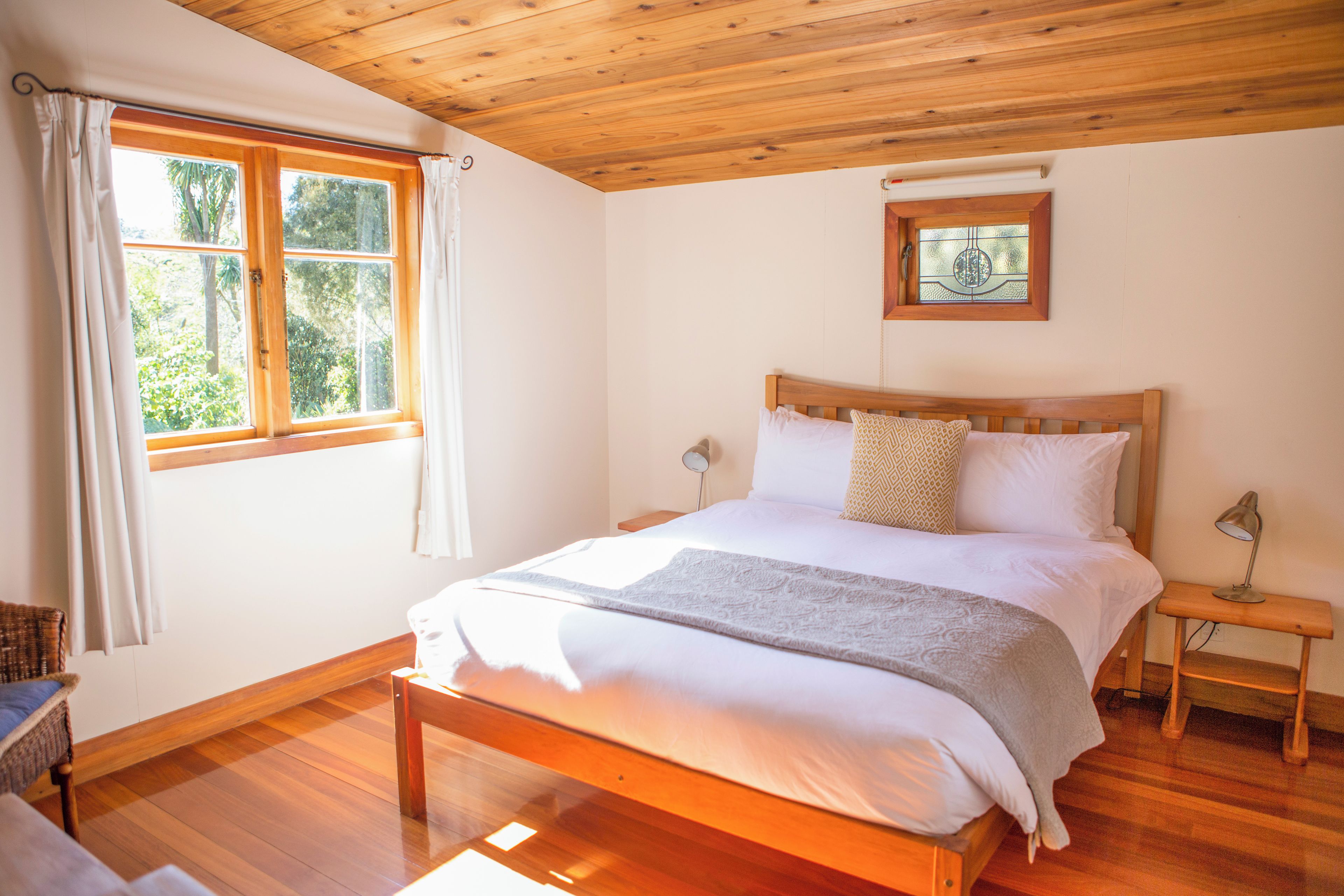 A bedroom with a wooden bed, a nightstand, a bedside lamp, a window with curtains, and a framed picture on the wall.