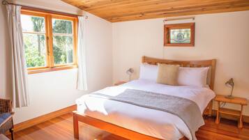 A bedroom with a wooden bed, a nightstand, a bedside lamp, a window with curtains, and a framed picture on the wall.