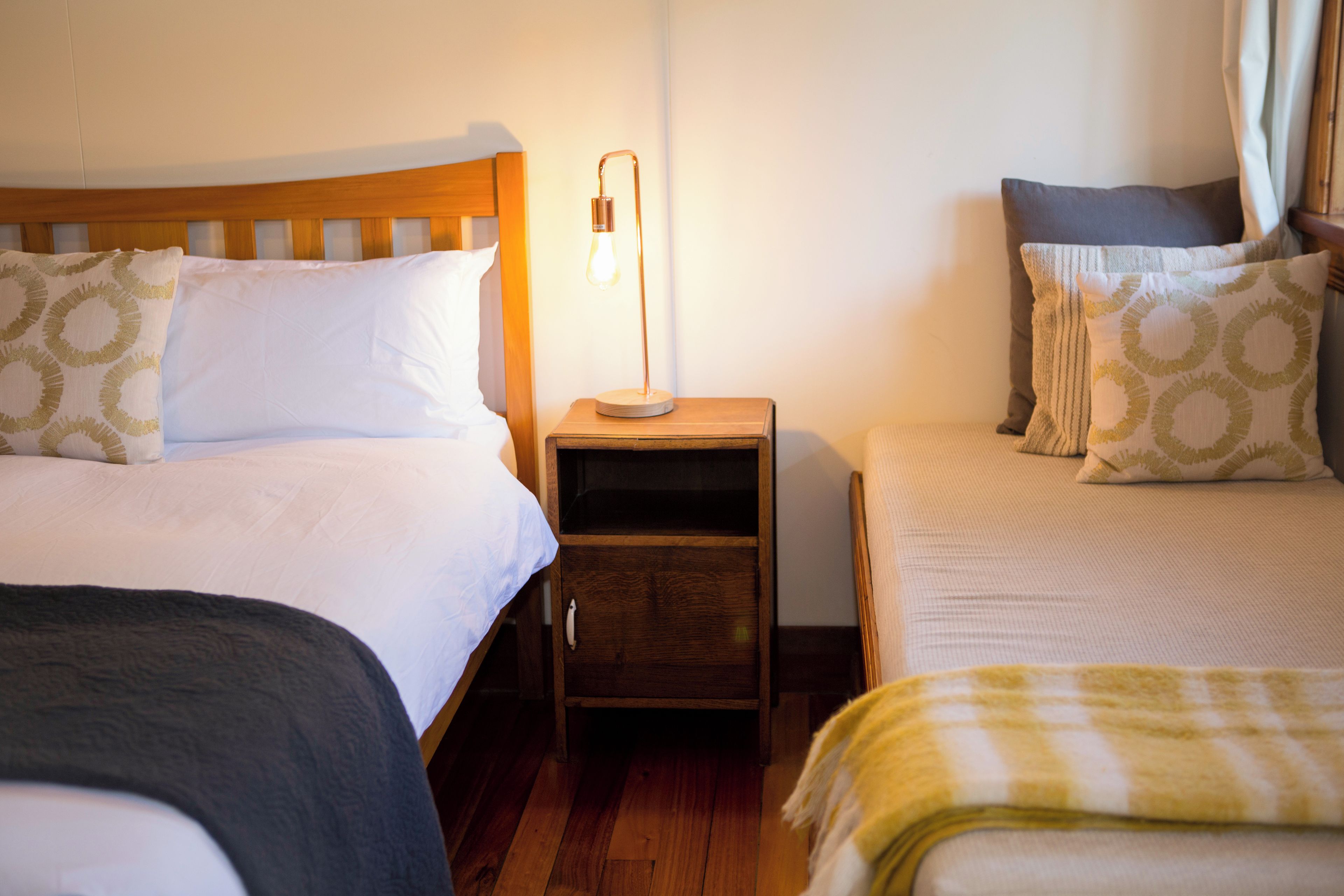 A hotel room with two single beds, a nightstand with a lamp, and a wooden floor.