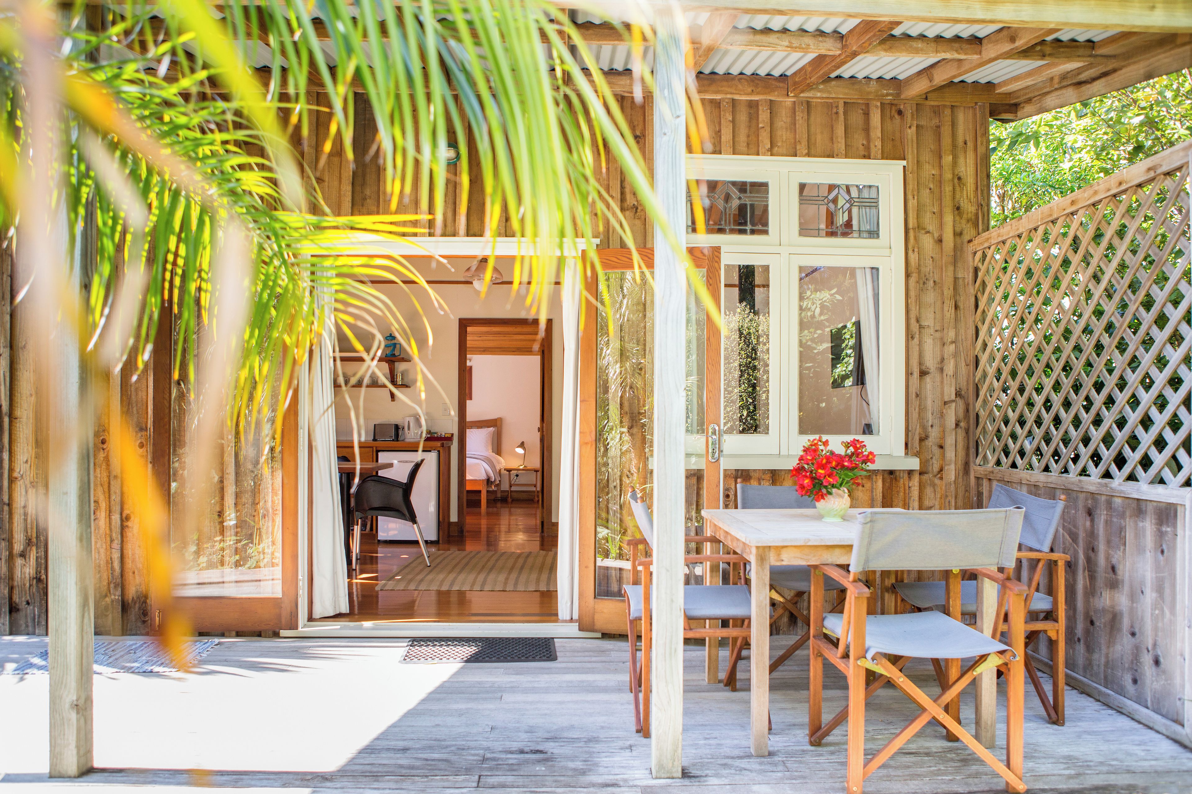 A wooden deck with a table and chairs, a door leading to a room, and a lattice fence.