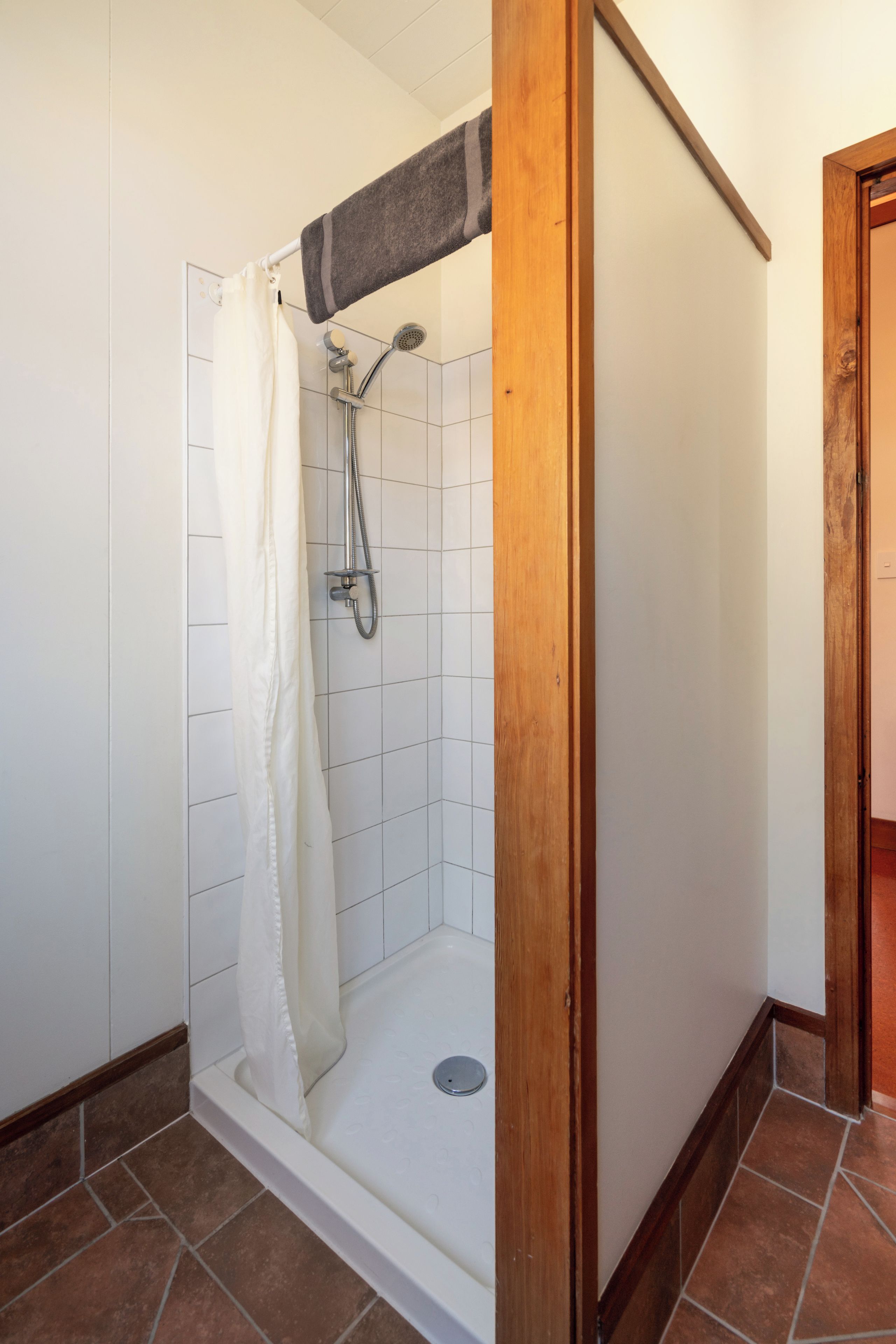 A shower area with a white curtain, a showerhead, and a drain.