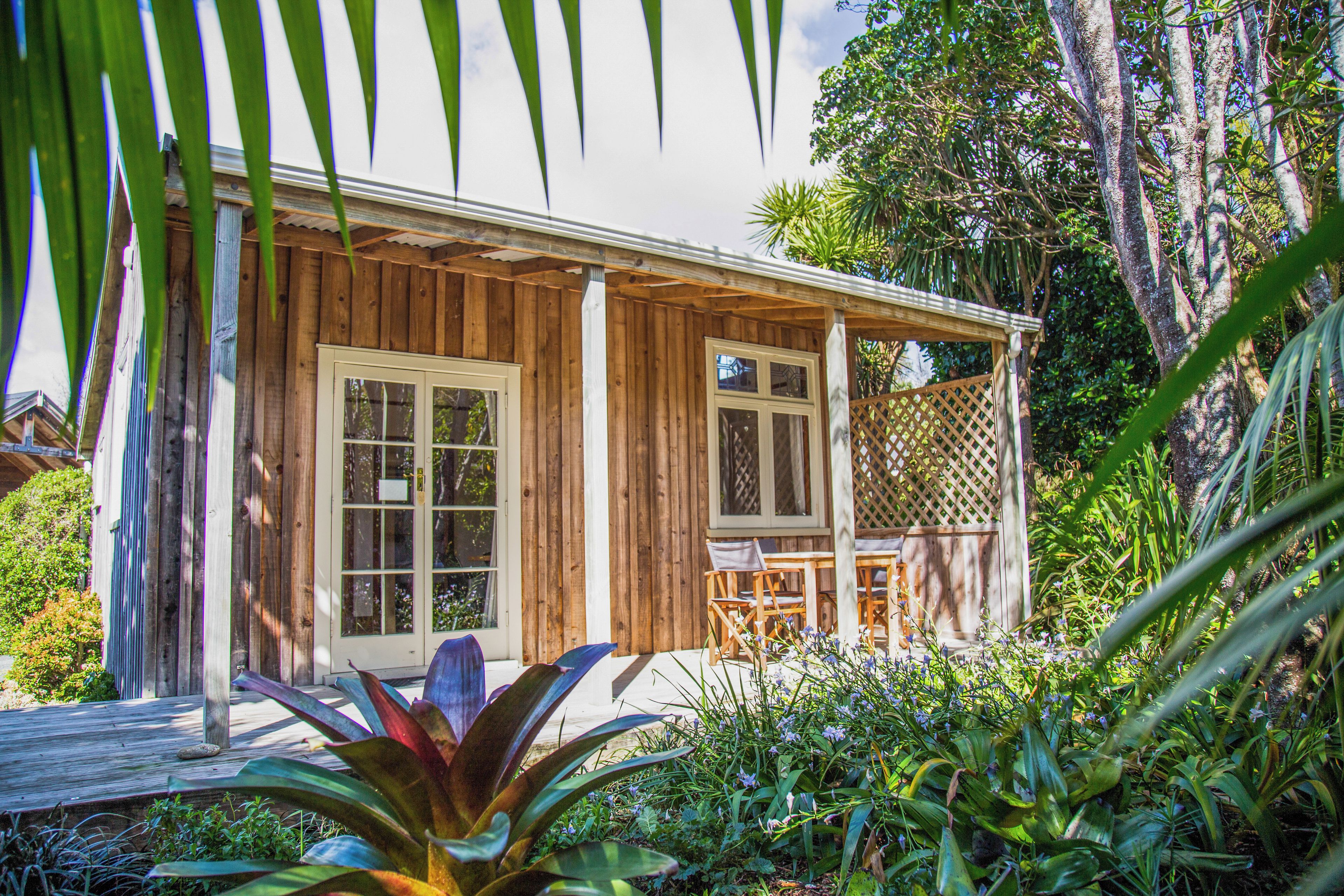 A wooden house with a porch, a small deck, and a garden with various plants and flowers.