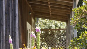 A wooden structure with a roof, surrounded by various plants and flowers. - Church Accommodation (Hahei)