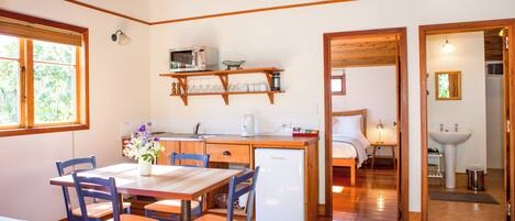 A compact kitchen with a dining area, wooden flooring, and a view into a bedroom.