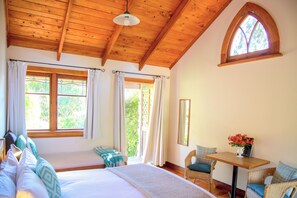 A room with a bed, two windows with curtains, a table with chairs, and a mirror on the wall. - Church Accommodation (Hahei)