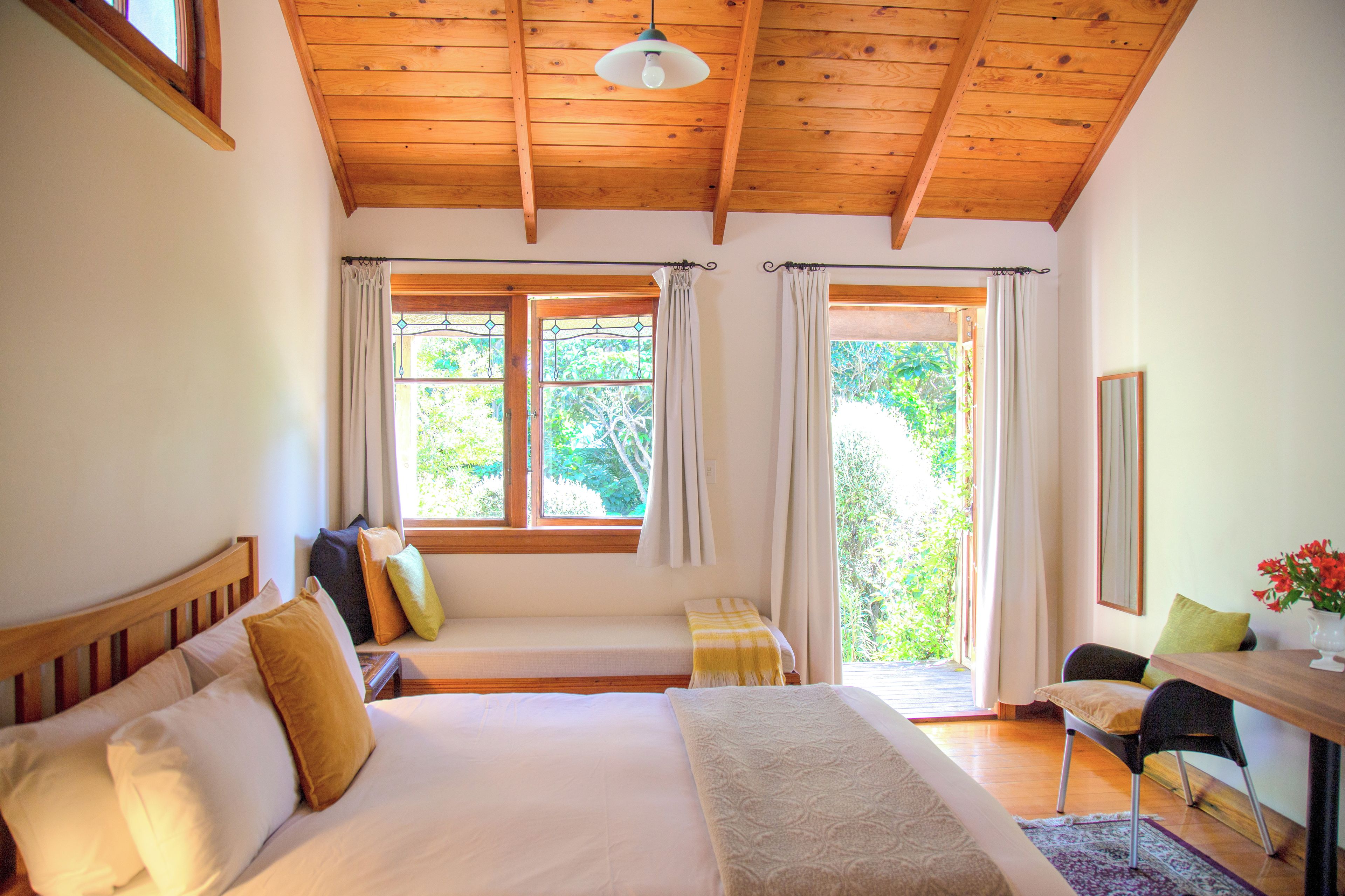 A bedroom with a bed, a bedside table, a chair, and two windows with curtains.