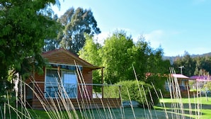Una cabaña de madera con balcón, rodeada de abundante vegetación y árboles.