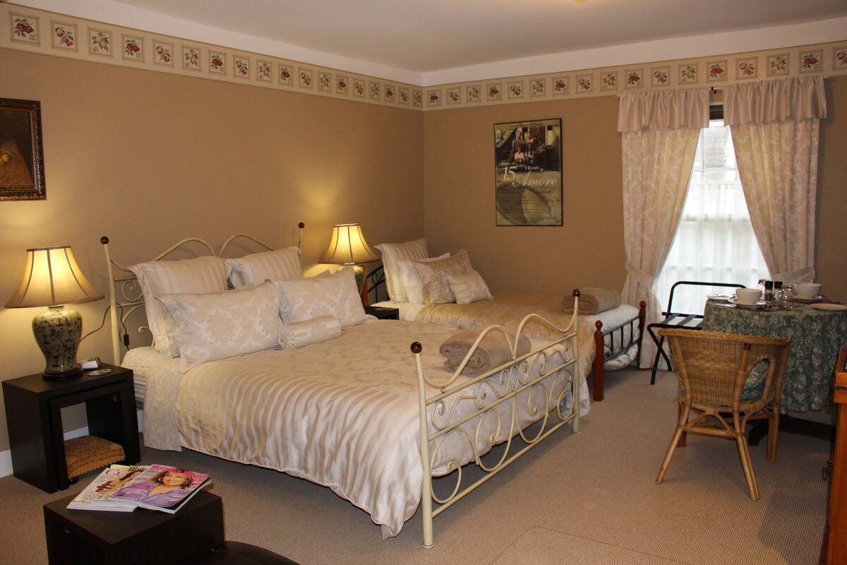 A bedroom with a bed, bedside tables, a chair, a small table, and a window with curtains.