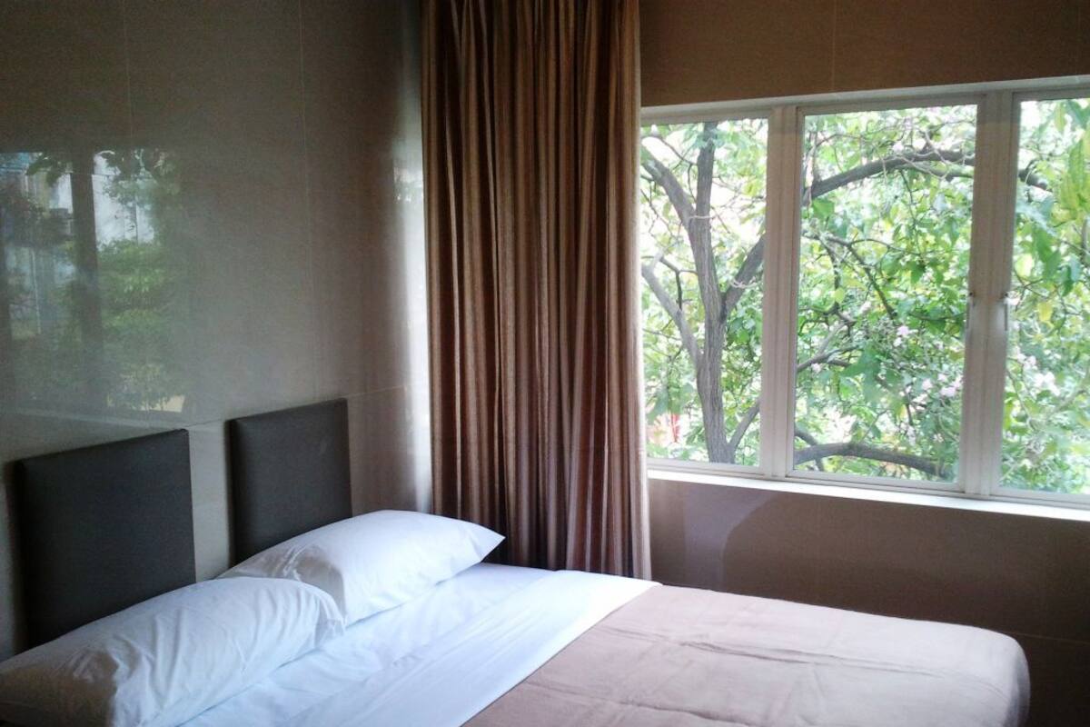 Ein Bett mit Kopfteil, ein Fenster mit Vorhängen und Blick auf Bäume.