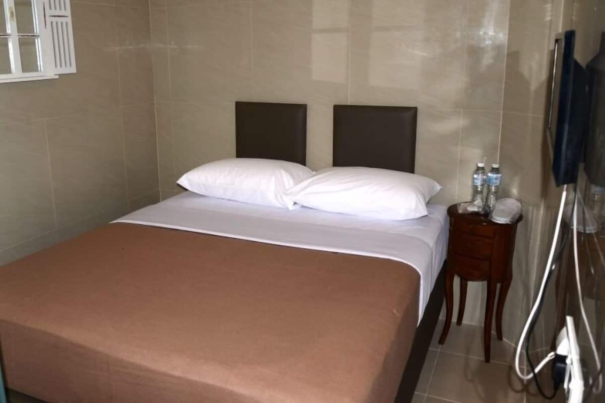 Ein Hotelzimmer mit einem Bett, Kissen, einem Nachttisch mit Pflegeartikeln und einem Handtuchhalter.