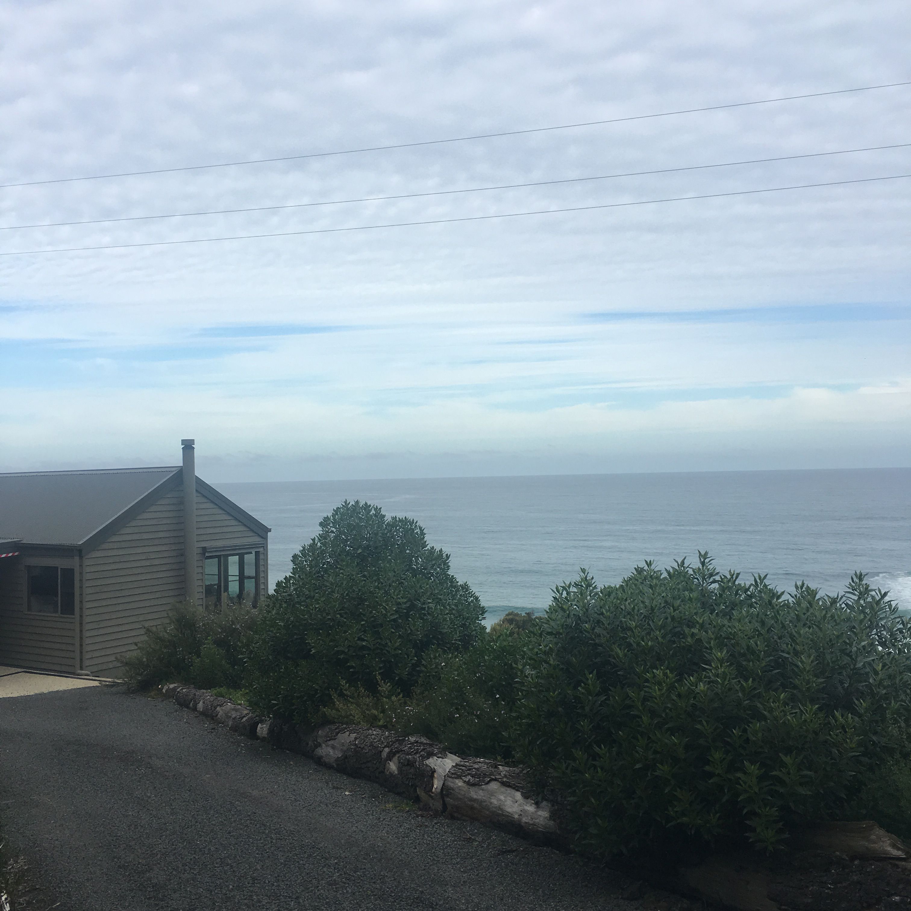 A coastal house with a view of the sea, a gravel driveway, and a stone retaining wall.