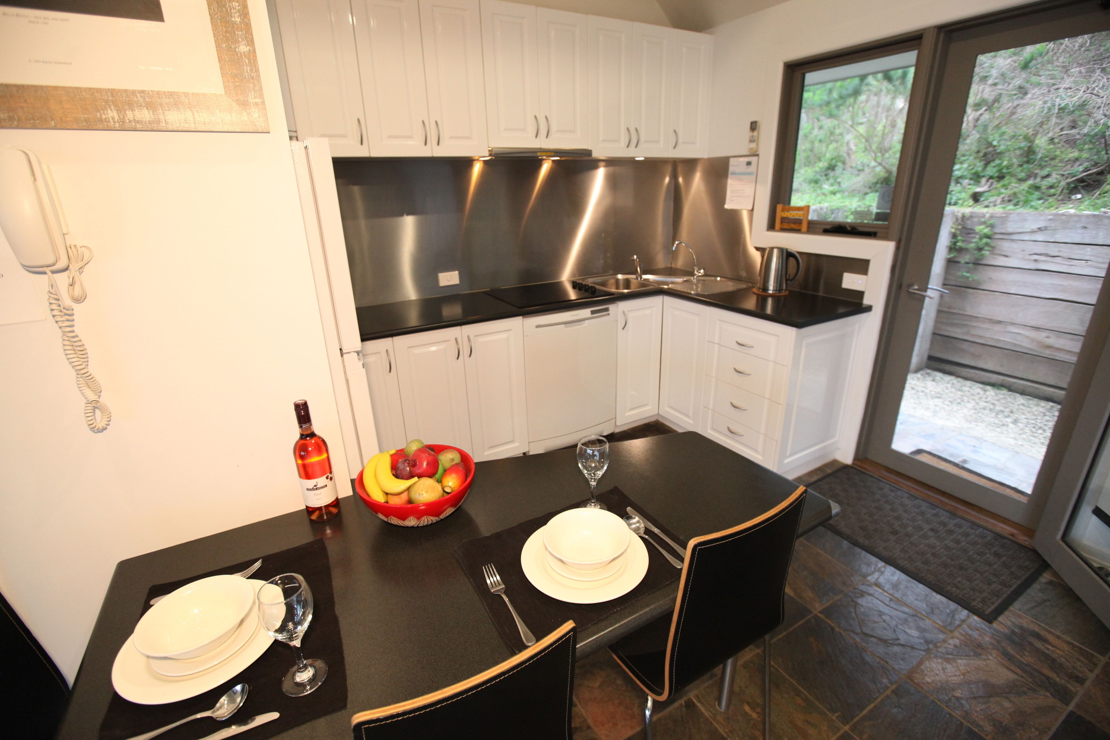 A modern kitchen with white cabinets, a black countertop, and a dining area set for two.