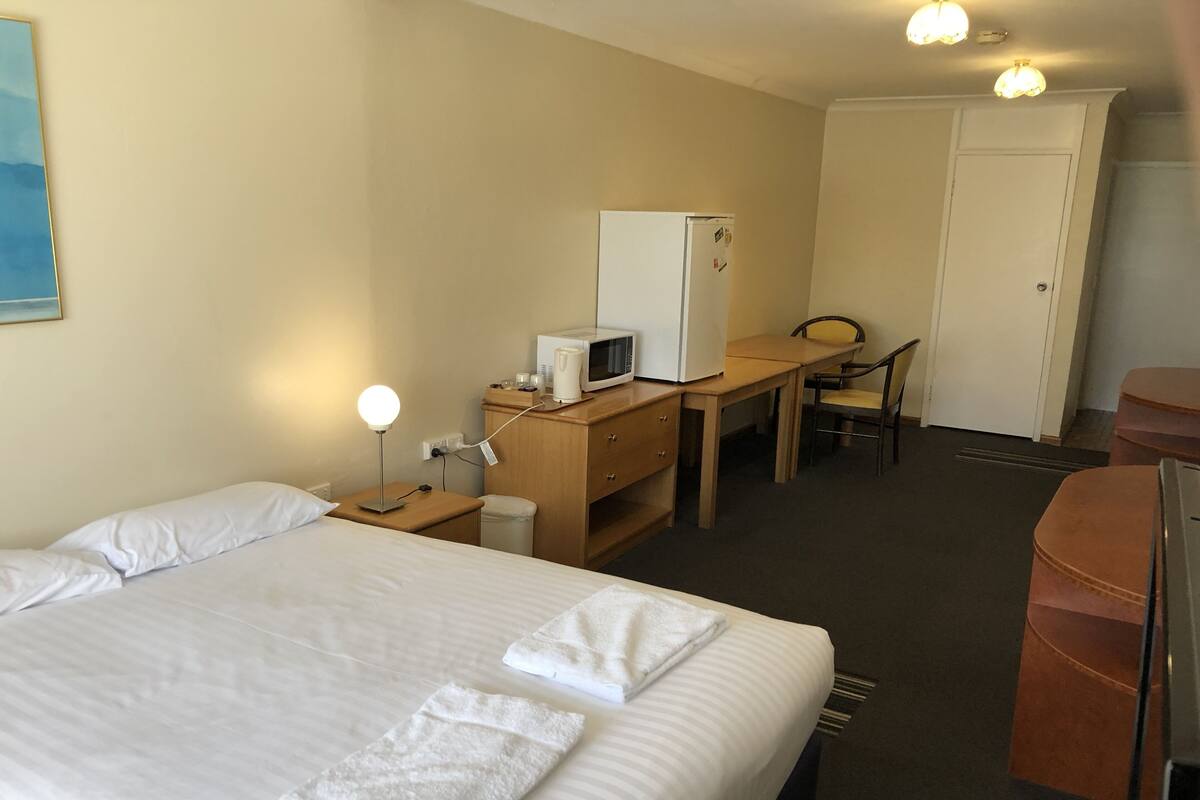 Ein Hotelzimmer mit einem Bett, einem Schreibtisch mit Mikrowelle, einem Sessel und einem Kleiderschrank.