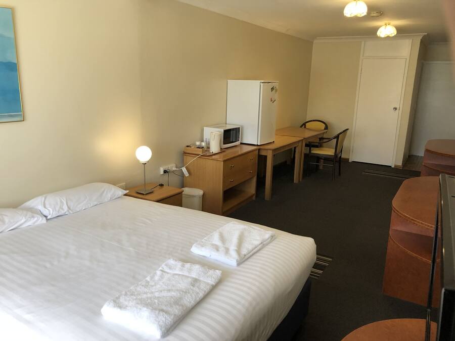 A hotel room with a bed, a desk with a microwave, a chair, and a wardrobe.