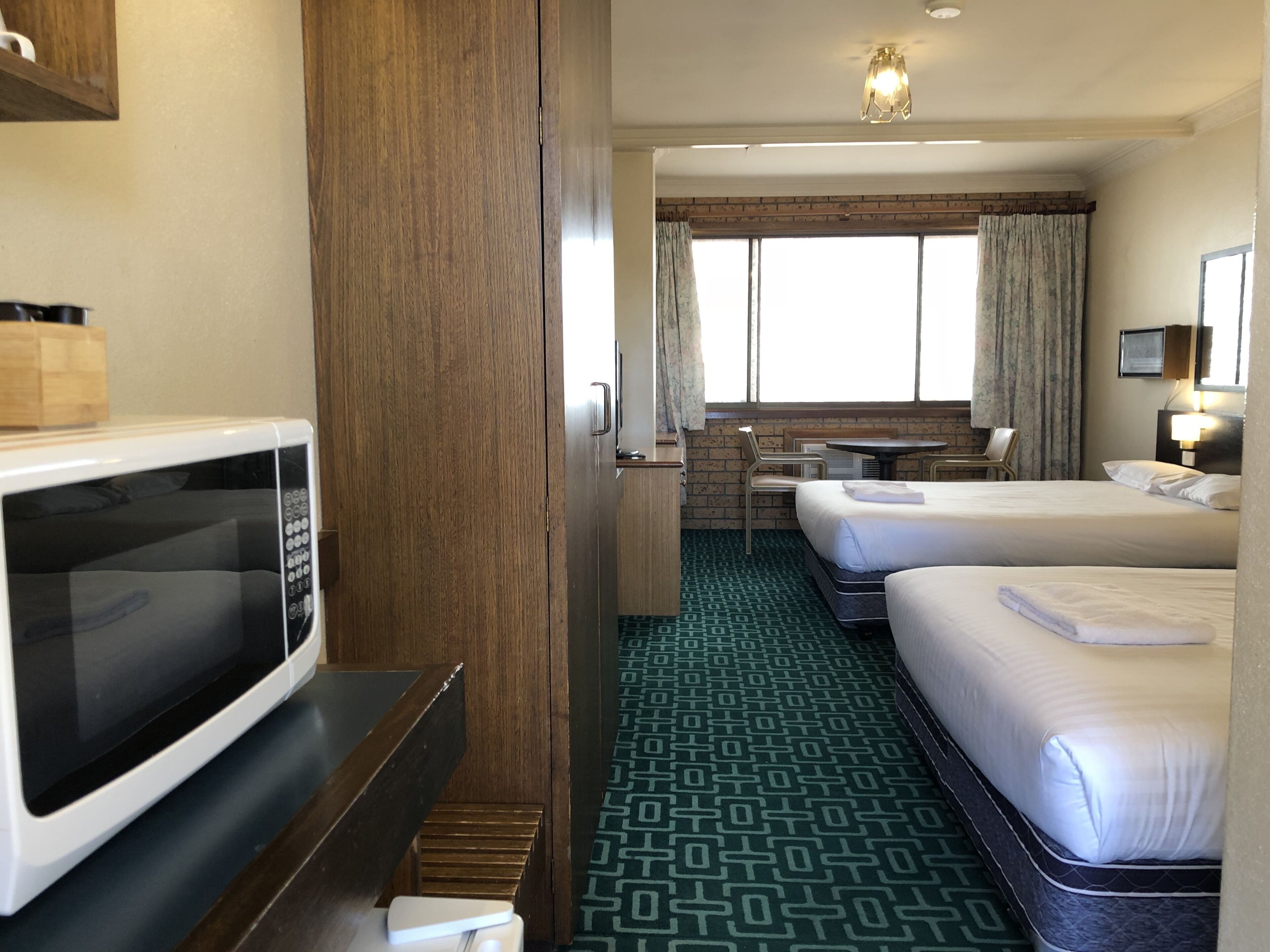 A hotel room with a microwave, a desk, two beds, a small table, and a window with curtains.