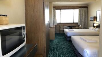 Habitación de hotel con microondas, escritorio, dos camas, una mesita pequeña y ventana con cortinas.