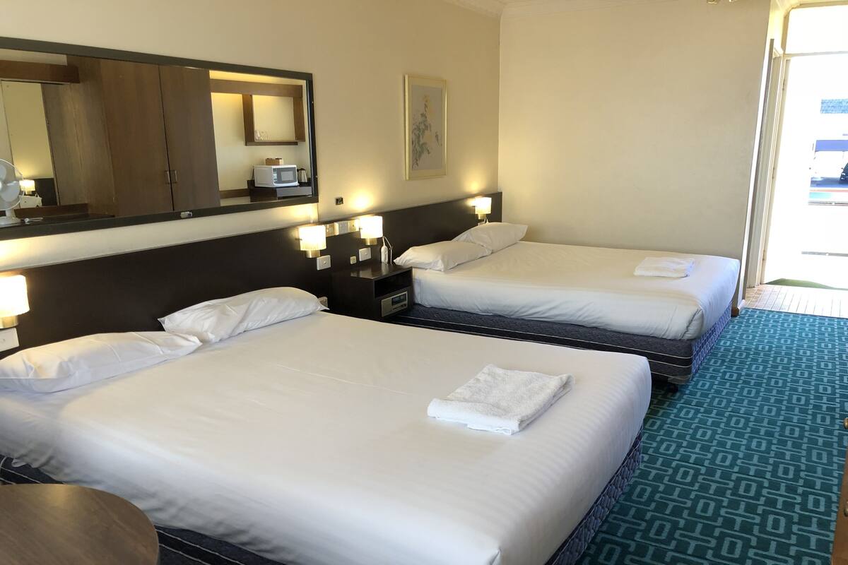 Ein Hotelzimmer mit zwei Betten, einem großen Spiegel, Nachttischlampen und Blick ins Freie.