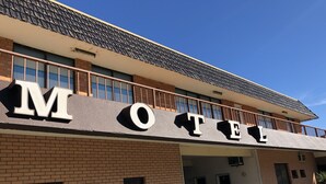Un motel con un llamativo letrero que dice 'Motel' en la fachada, que presenta un sencillo exterior de ladrillo y un techo plano.
