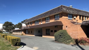 Un motel con fachada de ladrillo, zona de estacionamiento techada y cielo despejado.