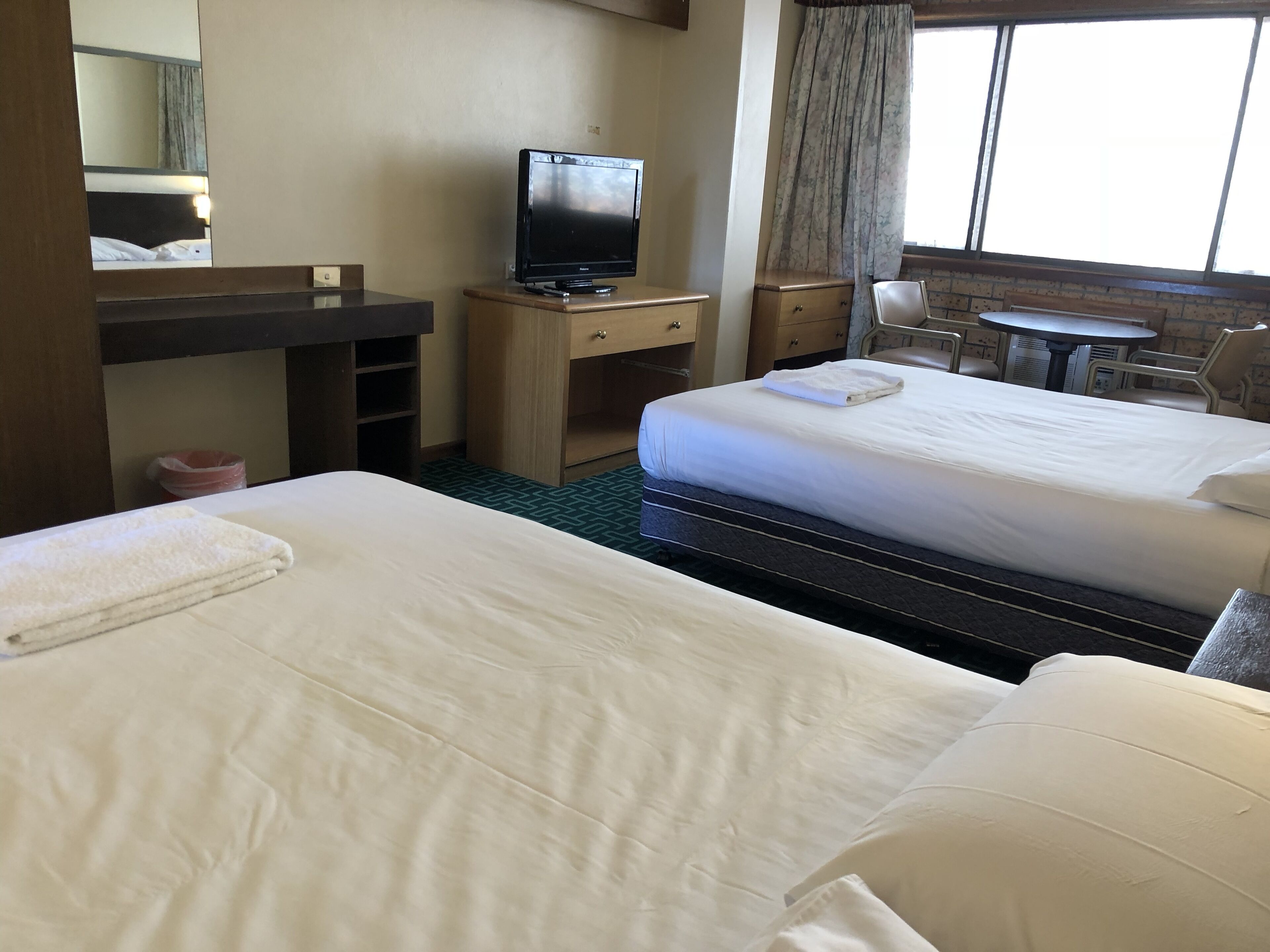 Una camera d'albergo con due letti, una scrivania con un computer, una sedia e un piccolo tavolo.