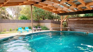 A clear swimming pool with a wooden pergola overhead, surrounded by a wooden fence and greenery. - Bayplay Beach Accommodation - 2 locations (Portsea)