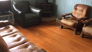 A living room with a brown leather sofa, a leather armchair, and a wooden coffee table. A television is on a white stand, and a wood-burning stove is in the corner. - Rangemore Estate (Moola)