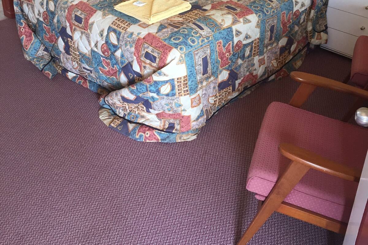 A bed with a colorful quilt, a bedside lamp, a nightstand, and a chair.