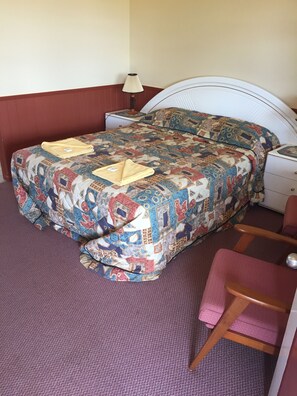 A bed with a colorful quilt, a bedside lamp, a nightstand, and a chair.