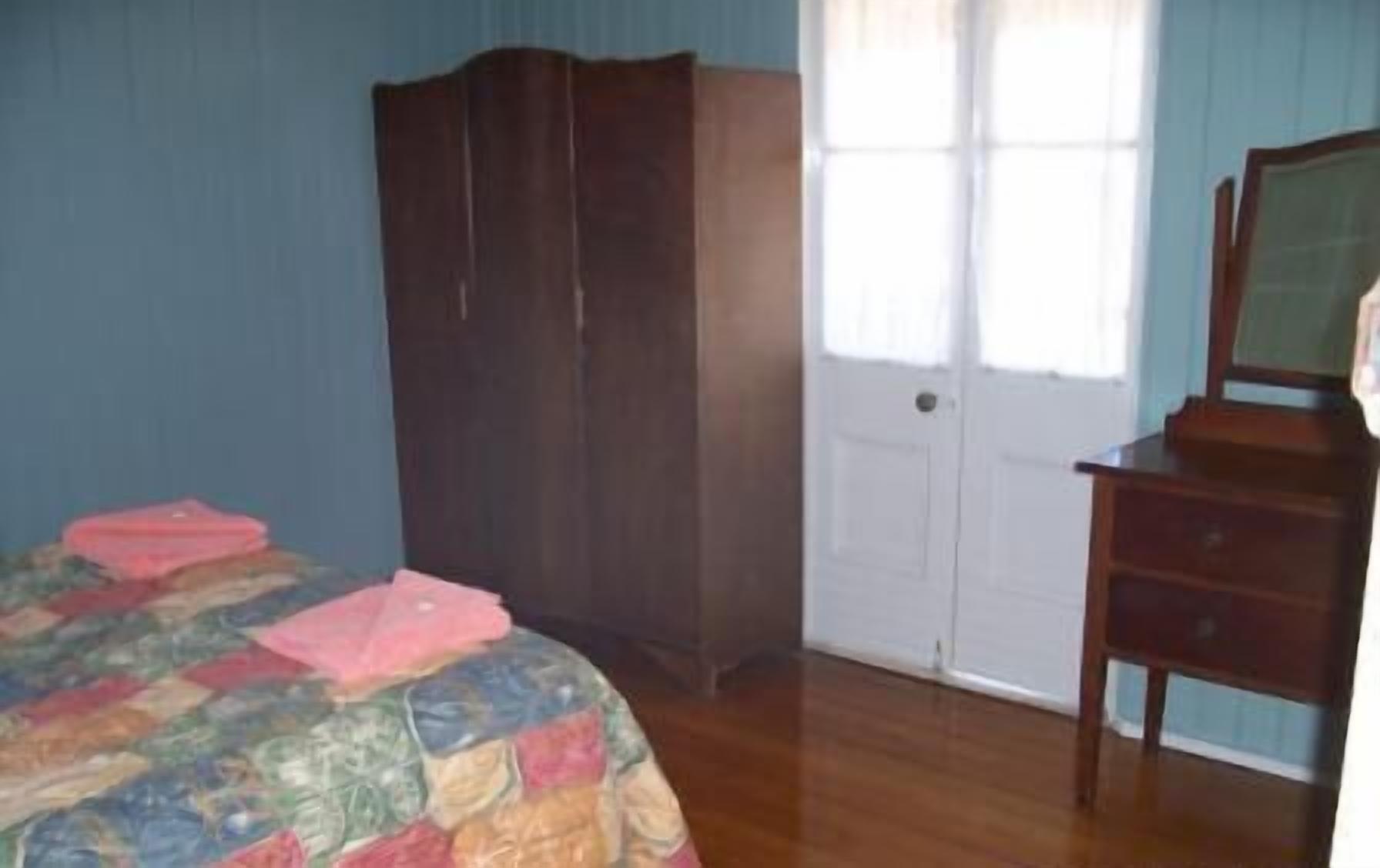 A bedroom with a bed, a wardrobe, a dresser, and a door with curtains.