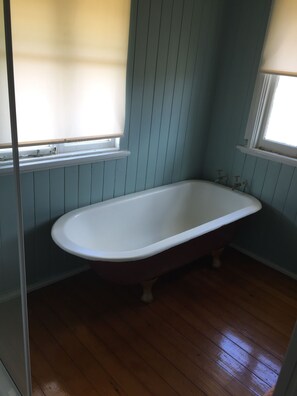 A bathroom with a freestanding bathtub, wooden flooring, and light blue paneled walls.