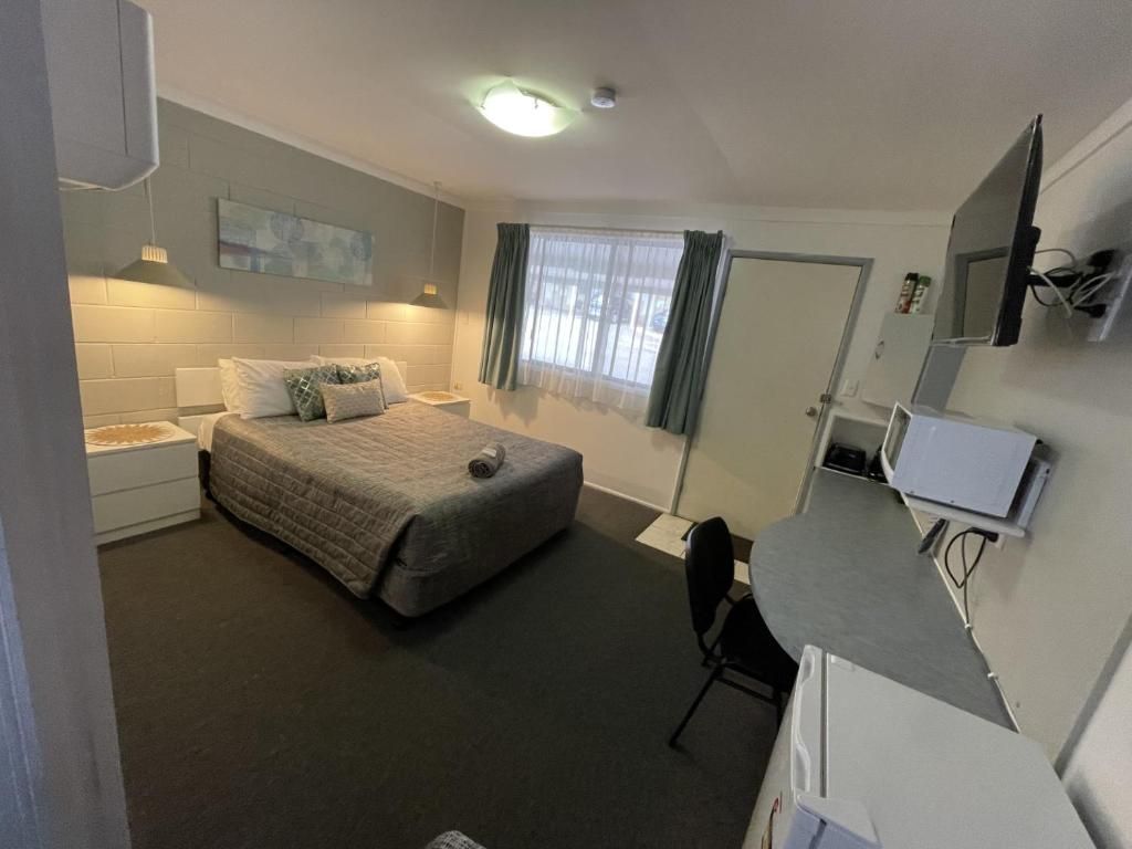 A hotel room with a bed, a desk, a chair, a television, and a door.