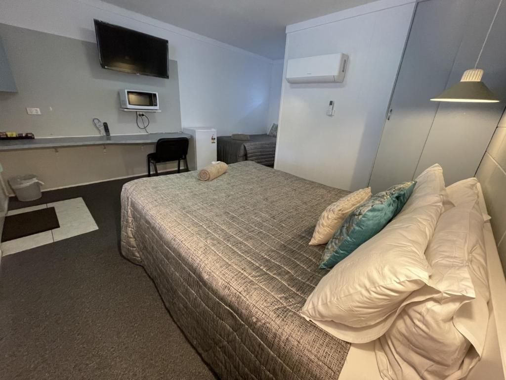 A hotel room with a bed, a desk, a chair, a television, and an air conditioning unit.