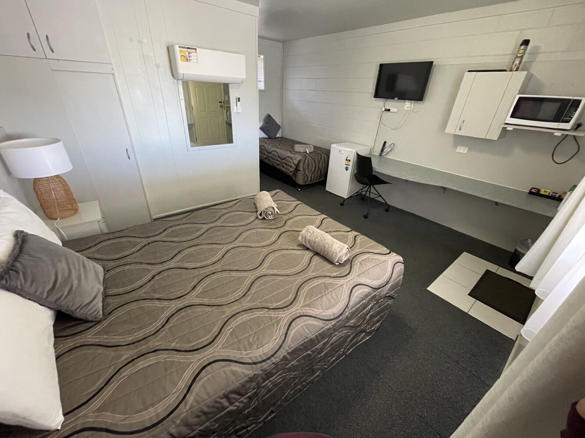 Una habitación de hotel con cama, escritorio, silla, televisor y microondas.