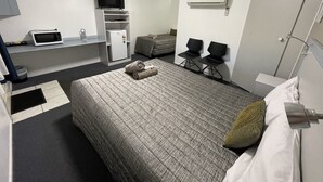 A compact hotel room with a bed, a TV, a microwave, a small fridge, and a seating area with chairs. - Hatton Vale Motel (Hatton Vale)