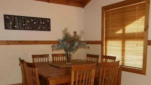 Un comedor con una mesa y sillas de madera, un jarrón con flores y una ventana con persianas.