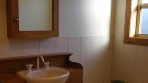 Un baño con tocador de madera, lavamanos, espejo y bañera.