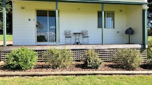 A single-story building with a covered porch, two chairs, a table, and a potted plant. - Promhills Cabins (Yanakie)