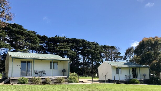 Two small, single-story mobile homes with a green roof, surrounded by a grassy area and trees. - Promhills Cabins (Yanakie)