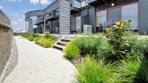 Een modern gebouw met een grindpad, terrasplekken en groen.