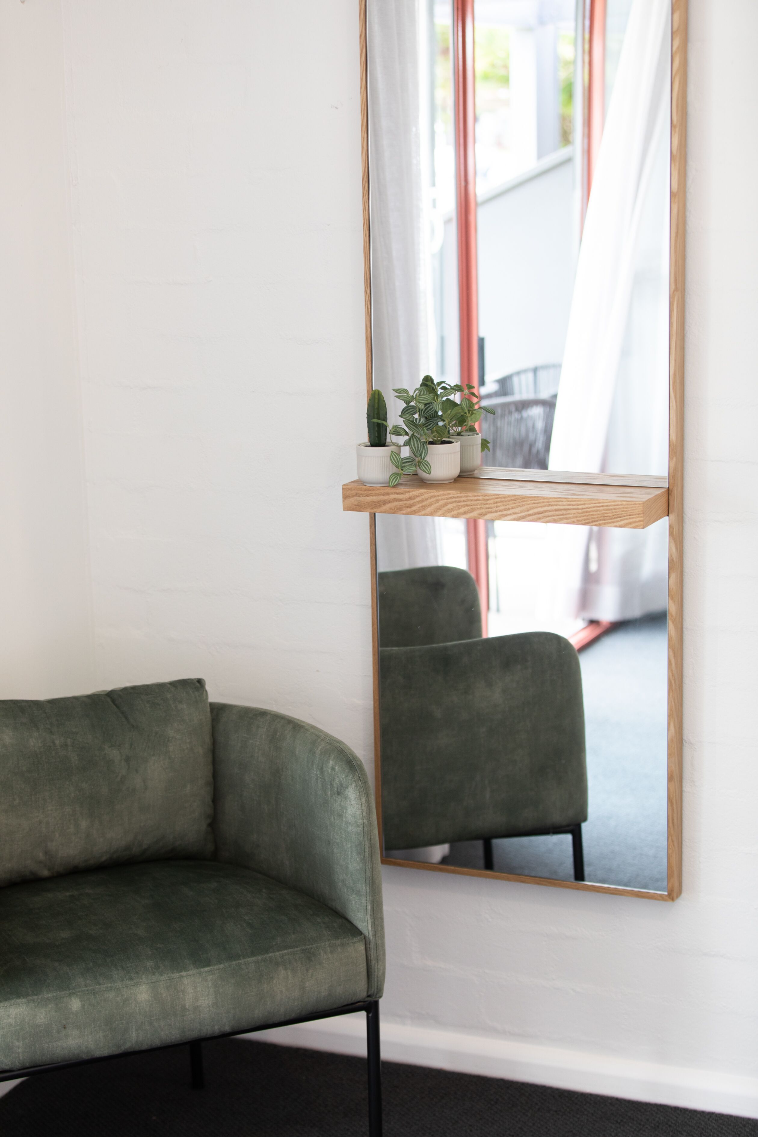 A room with a green armchair, a mirror with a wooden frame, and a shelf with potted plants.