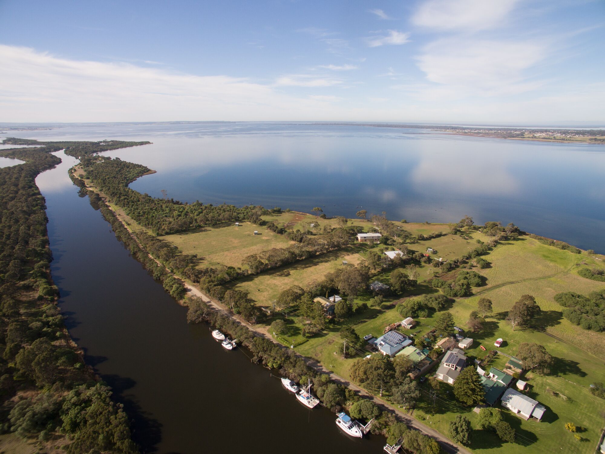 Vista aérea de una propiedad junto al lago con barcos amarrados a la orilla, rodeada de vegetación y edificios residenciales.