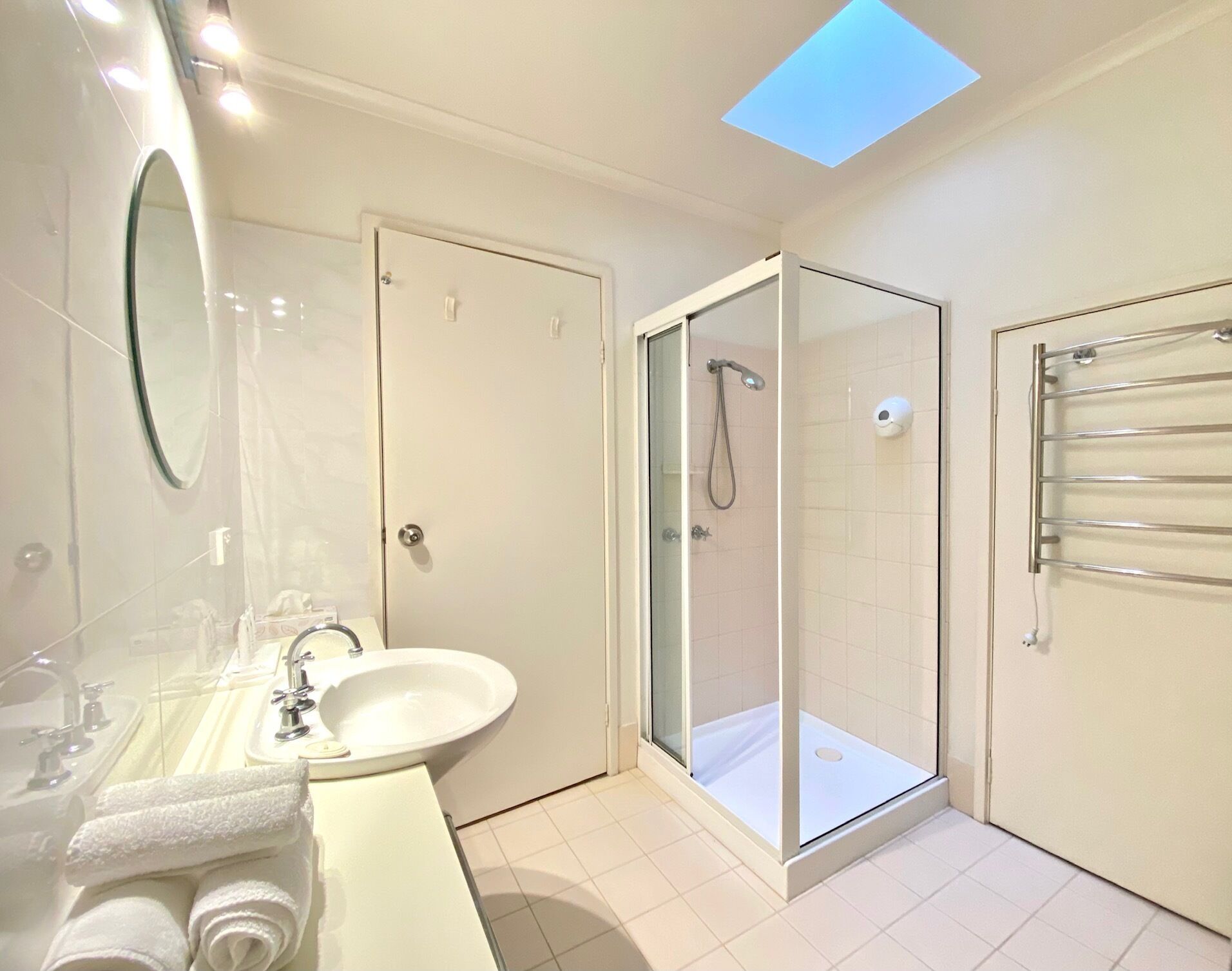 Un baño moderno con ducha envuelta en cristal, un lavamanos con espejo y un perchero para toallas.