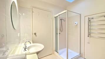 Un baño moderno con ducha envuelta en cristal, un lavamanos con espejo y un perchero para toallas.