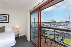 A hotel room with a balcony, a bed, a nightstand, and a view of a marina with boats. - Mariners Cove at Paynesville Motel & Apartments (Paynesville)