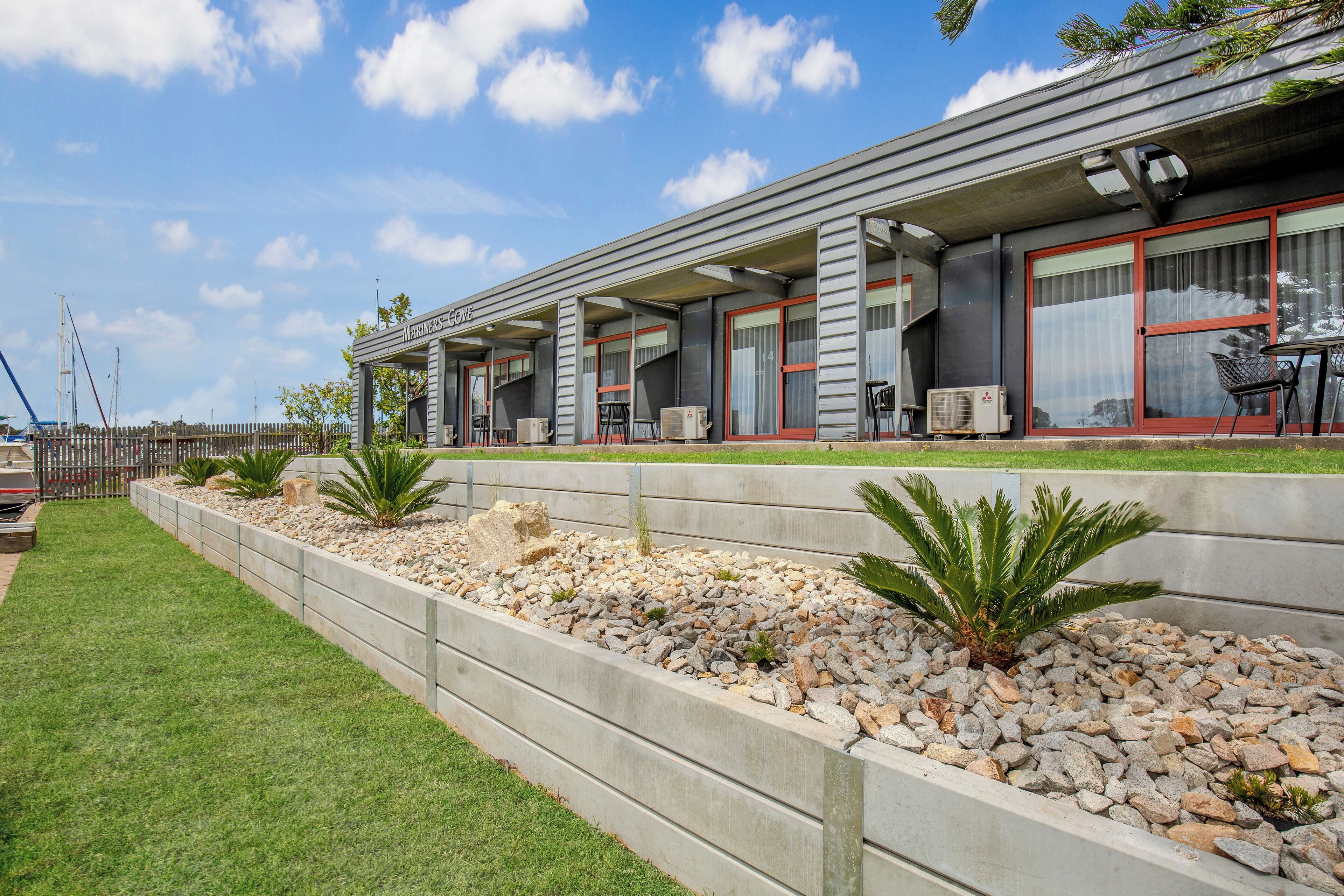 A modern hotel with a flat roof, large windows, and a well-maintained garden area with rocks and plants.
