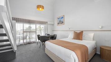 A hotel room with a bed, a desk, and a chair. There is a staircase leading to an outdoor area.