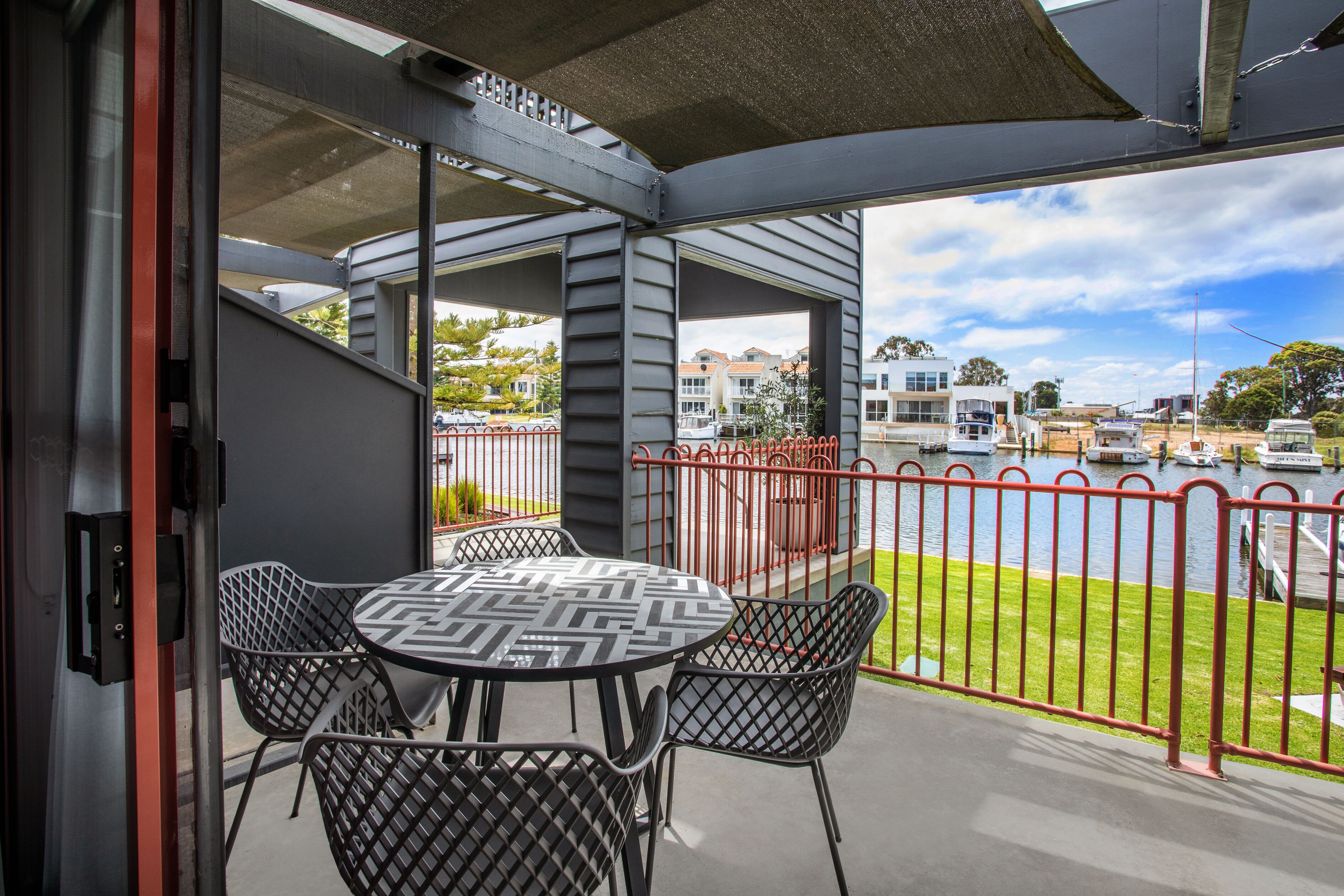An outdoor seating area with a table and chairs, a view of a marina with boats, and a red railing.